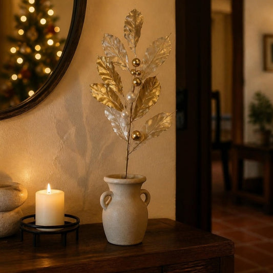 Vara de Ámbar Navideño 75 cm Dorada — hojas doradas en un florero de cerámica junto a una vela encendida