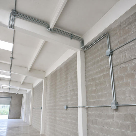 Tubo conduit EMT galvanizado 2 pulg — fijado con abrazaderas en el techo y la pared de una bodega